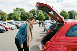 Jeune femme souriante inspectant le coffre d'une voiture neuve