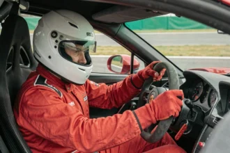 Pilote en combinaison rouge au volant d'une voiture de sport sur circuit lors d'un stage de pilotage
